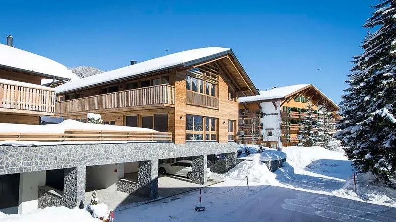 Modernes Holzchalet mit Steinsockel und Balkonen, umgeben von Schnee und Bergen.
