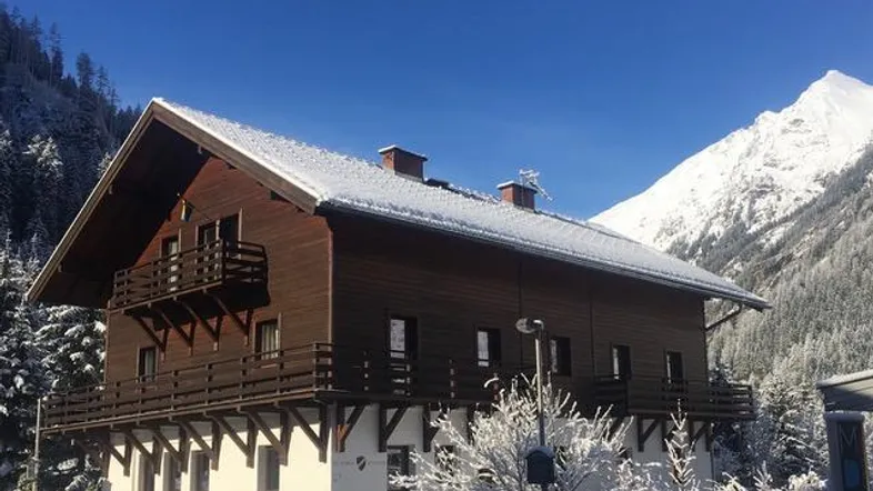 Traditionelles Holzhaus im alpinen Stil mit schneebedecktem Dach und Bergblick.