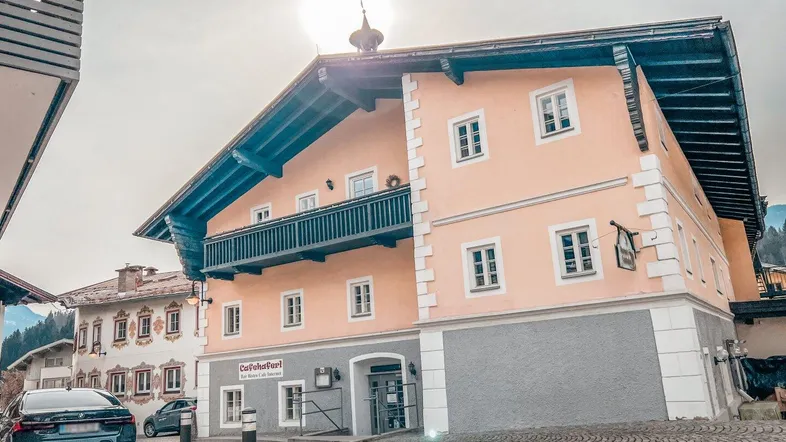Traditionelles Gebäude mit Balkon und hellrosa Fassade an einer gepflasterten Straße unter strahlendem Himmel.