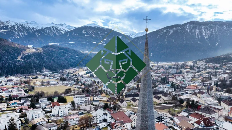 Panoramablick auf eine malerische Stadt mit schneebedeckten Bergen im Hintergrund und einem Kirchturm im Vordergrund.