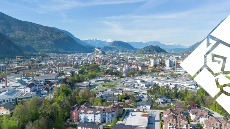Luftaufnahme einer Stadt mit Wohngebäuden, Industriegebieten und Bergen im Hintergrund unter blauem Himmel.