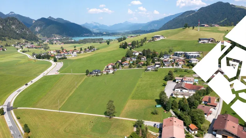 Luftaufnahme eines malerischen Dorfes in einem Tal mit Bergen und einem See im Hintergrund.