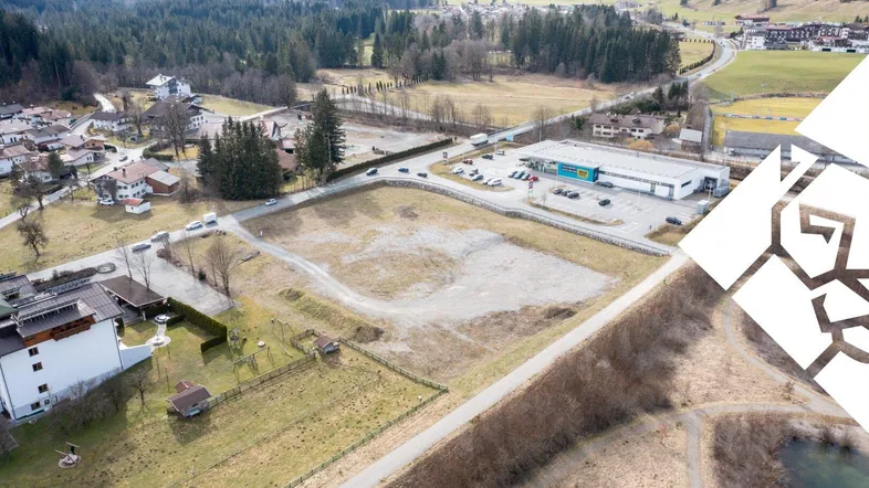 Luftaufnahme eines großen Baugrundstücks in ländlicher Umgebung mit angrenzendem Gewerbegebiet und Bergblick.
