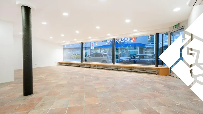 Großer, leerer Geschäftsraum mit großen Schaufenstern zur Straße und Terrakotta-Fliesenboden.