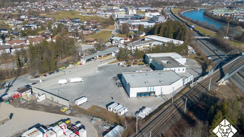 Weitläufige Luftaufnahme eines Industriegebiets mit Gebäuden, Parkflächen und einer Autobahn im Hintergrund.