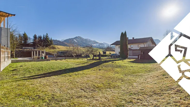 Weitläufiger Gartenbereich mit grüner Rasenfläche und malerischem Bergblick unter strahlendem Sonnenschein.