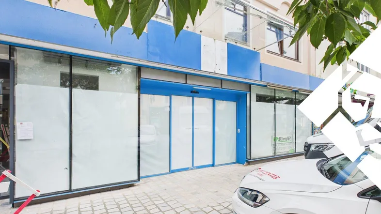 Außenansicht eines Geschäftsgebäudes mit blauer Fassadenverkleidung, großen Schaufenstern und automatischen Türen.