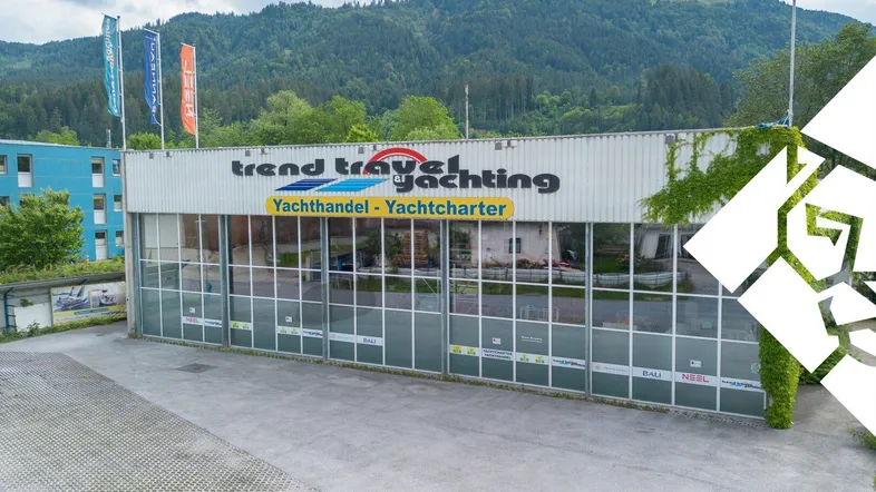 Ansicht des Geschäftsgebäudes mit großer Glasfassade und Beschilderung, umgeben von Bergen und einem Parkplatz.