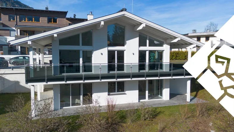 Modernes Einfamilienhaus mit großen Glasflächen, Balkon und Blick auf die umliegende Berglandschaft.
