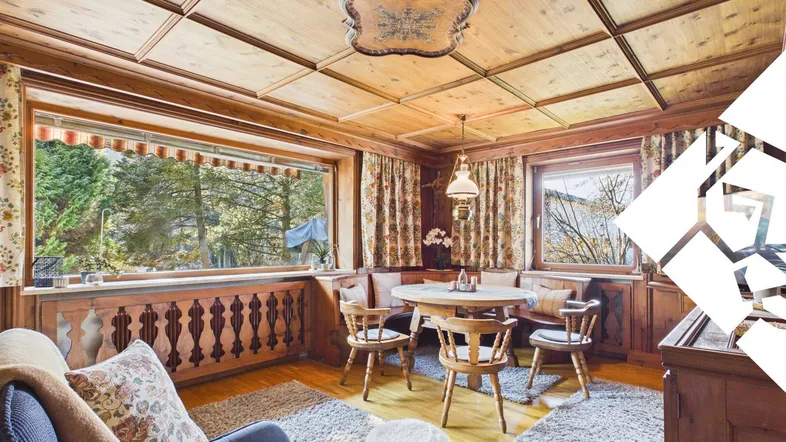 Gemütlicher Wohn-Essbereich im alpenländischen Stil mit Holztäfelung, Kassettendecke und Blick ins Grüne.