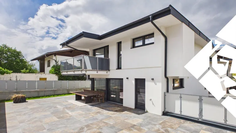 Moderne Villa mit großer gepflasterter Terrasse und Balkon, ideal für entspannte Stunden im Freien.