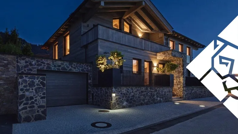 Modernes Chalet im alpinen Stil bei Nacht, mit beleuchteter Fassade und Garage.