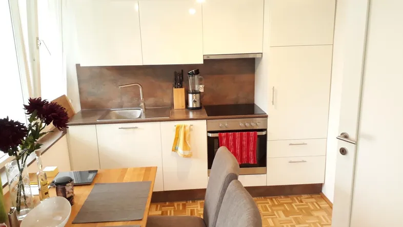 Helle Einbauküche mit weißen Hochglanzfronten, integriertem Backofen und Essbereich.