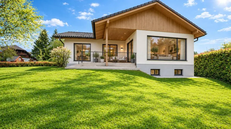 Modernes Einfamilienhaus mit großer Rasenfläche und überdachter Terrasse unter blauem Himmel.