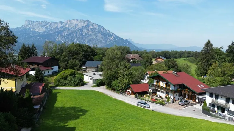 Panoramablick auf eine ländliche Siedlung mit Bergen im Hintergrund und grünen Wiesen.