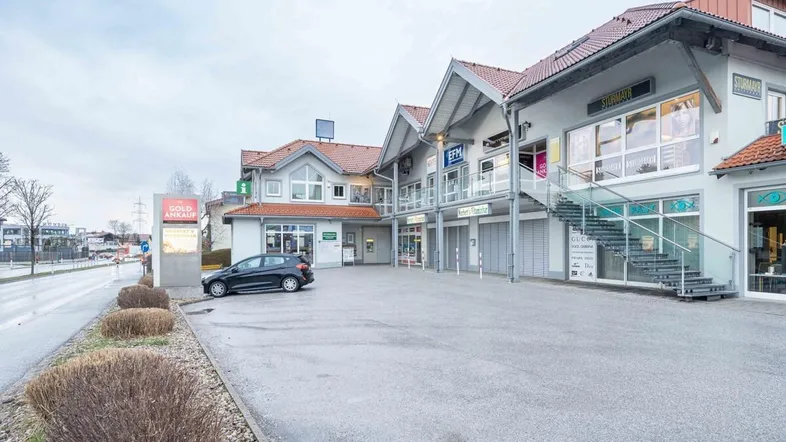 Außenansicht eines modernen Geschäftsgebäudes mit Parkplätzen und verschiedenen Ladenlokalen.