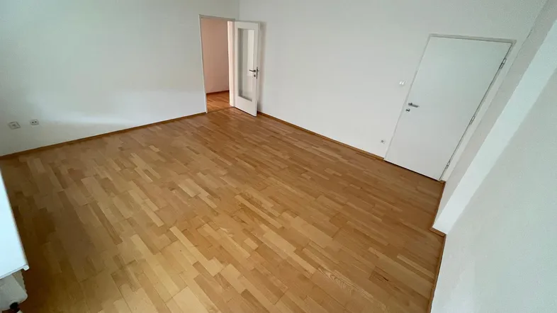 Helles Zimmer mit Holzparkettboden und weißen Wänden, bereit zur individuellen Gestaltung.