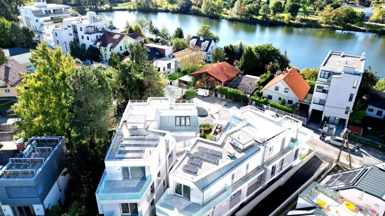 Luftaufnahme moderner Wohngebäude mit Flachdächern und Photovoltaikanlagen am Flussufer.
