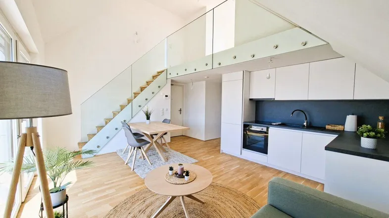Heller offener Wohn-Essbereich mit integrierter Küche, Holzfußboden und moderner Treppe zum Obergeschoss.