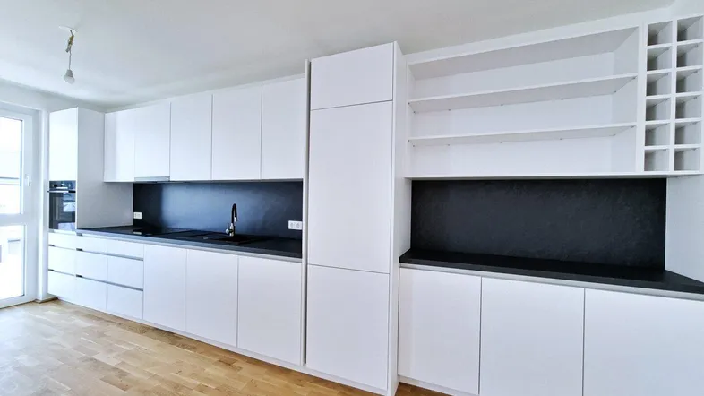 Moderne, helle Küche mit weißen Schränken, dunkler Arbeitsplatte und Holzfußboden in einem offenen Wohnbereich.