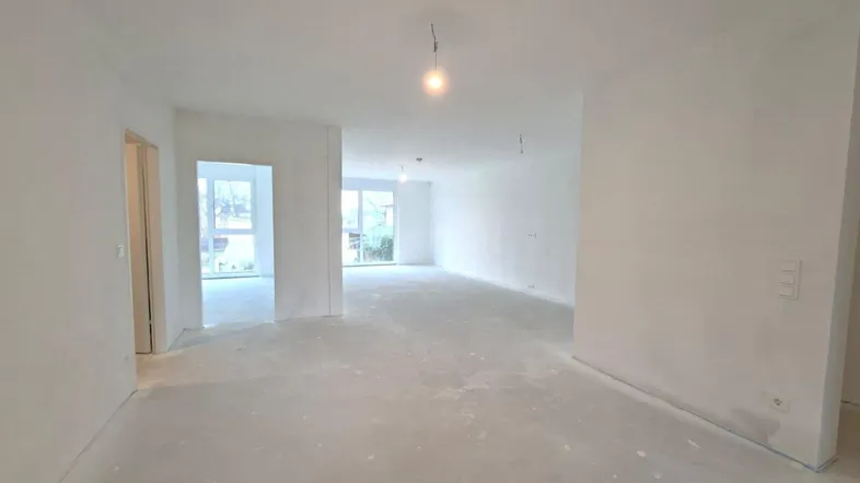 Geräumiger, unfertiger Wohnbereich mit großen Fenstern und viel Tageslicht, bereit für den Ausbau.