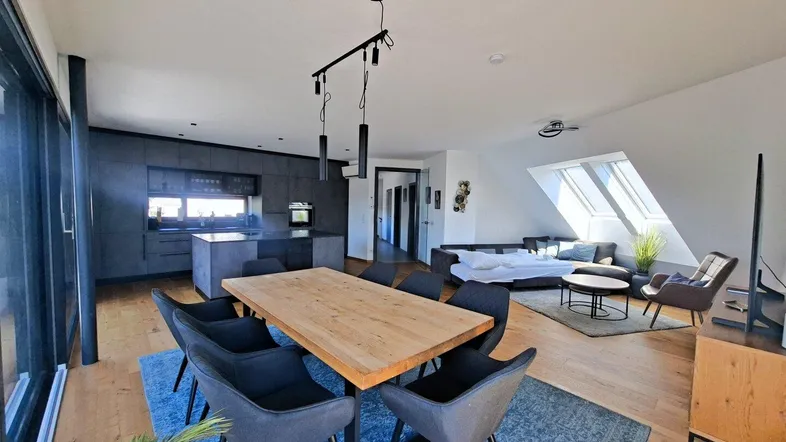Geräumiger offener Wohn- und Essbereich mit moderner Küche, Holzboden und Zugang zur Terrasse.