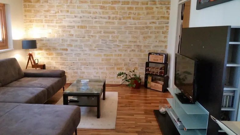 Gemütliches Wohnzimmer mit L-förmigem Sofa, Holzboden und einer dekorativen Ziegelwand.