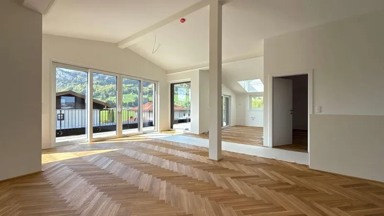 Helles, offenes Wohnzimmer mit Fischgrätparkett, hohen Decken und Zugang zu einem Balkon mit Bergblick.