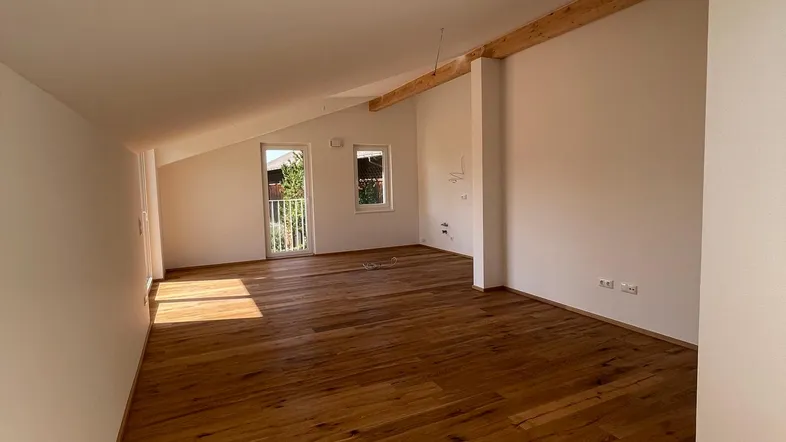 Heller Dachgeschossraum mit Holzboden, sichtbarem Holzbalken und Zugang zu einem Balkon.