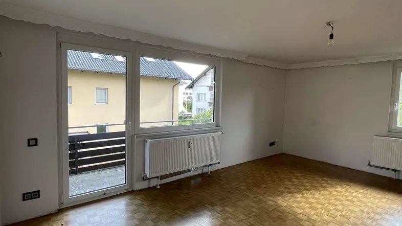 Helles, leeres Wohnzimmer mit Parkettboden und Zugang zu einem Balkon, bereit zur individuellen Gestaltung.