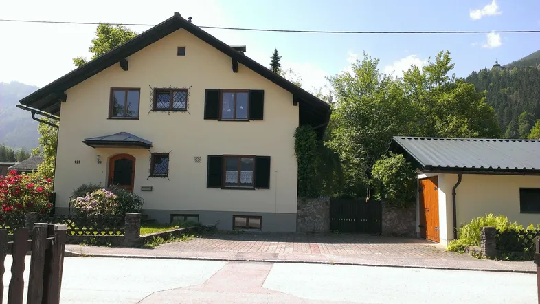 Traditionelles Einfamilienhaus mit Satteldach, grüner Umgebung und Blick auf die Berge.