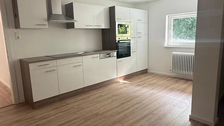Moderne Einbauküche mit weißen Schränken, Holzarbeitsplatte und integrierten Geräten in einem hellen Raum.
