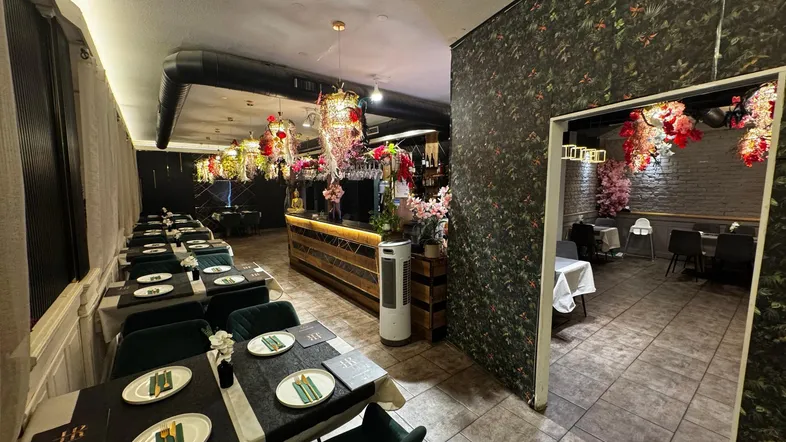 Geräumiger Restaurantbereich mit elegant gedeckten Tischen, einer Bar und auffälliger floraler Dekoration an der Decke.