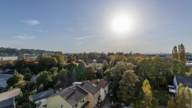 Weitläufiger Blick über die Stadt und grüne Baumlandschaft unter strahlend blauem Himmel.