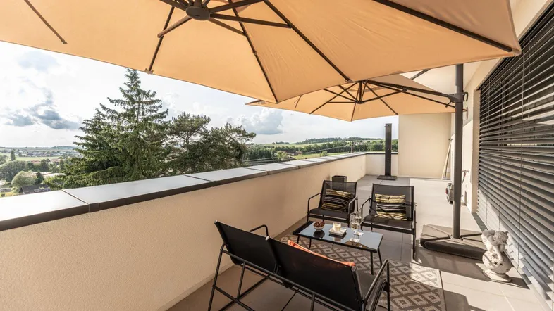 Geräumige Dachterrasse mit bequemen Gartenmöbeln und Sonnenschirmen, ideal für entspannte Stunden im Freien mit Weitblick.