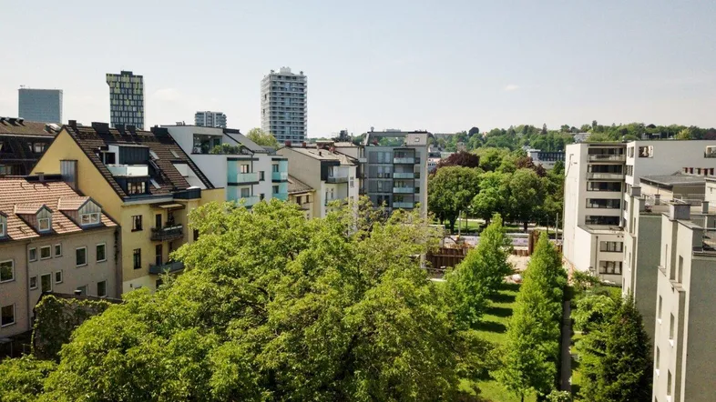 Weitläufiger Blick über die Stadt mit viel Grün und modernen Gebäuden im Hintergrund.