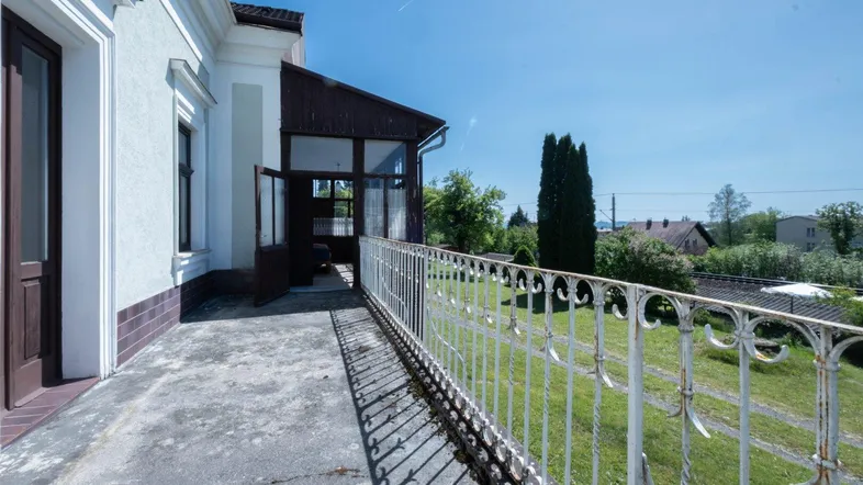 Alter Balkon mit schmiedeeisernem Geländer und Blick ins Grüne.