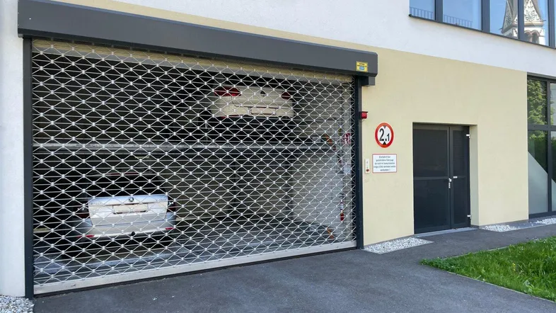 Einfahrt zur Tiefgarage mit Rolltor und zwei parkenden Autos im Inneren des Gebäudes.