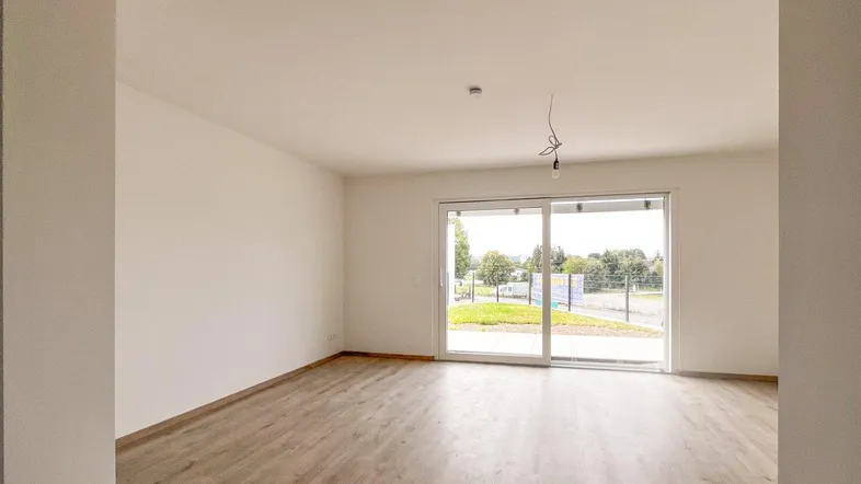 Helles, leeres Wohnzimmer mit modernem Laminatboden und großer Schiebetür zur Terrasse.