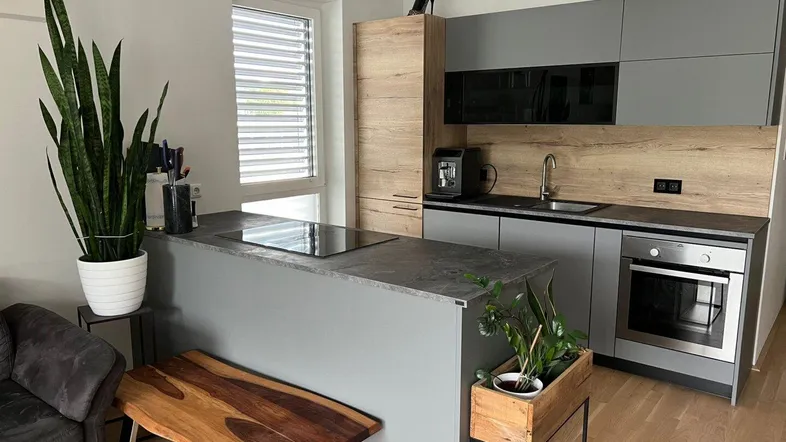 Moderne Küche mit grauen und holzfarbenen Schränken, einer Kochinsel mit Induktionskochfeld und einem Fenster.