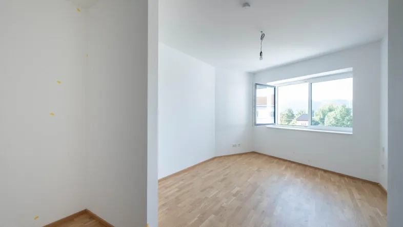 Helles, leeres Zimmer mit Parkettboden und großen Fenstern, bereit für die individuelle Gestaltung.