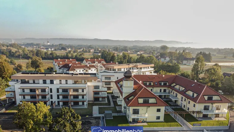 Luftaufnahme eines modernen Wohnkomplexes mit traditionellem Gebäude und grüner Umgebung.