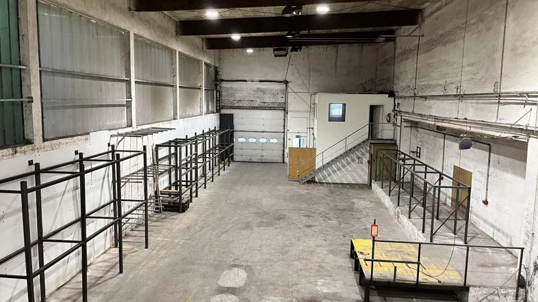 Große, leere Lagerhalle mit Betonboden, hohen Decken und einem Rolltor am Ende des Raumes.