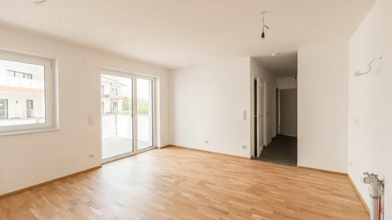Heller Wohnbereich mit Parkettboden, weißen Wänden und Zugang zu einem Balkon.