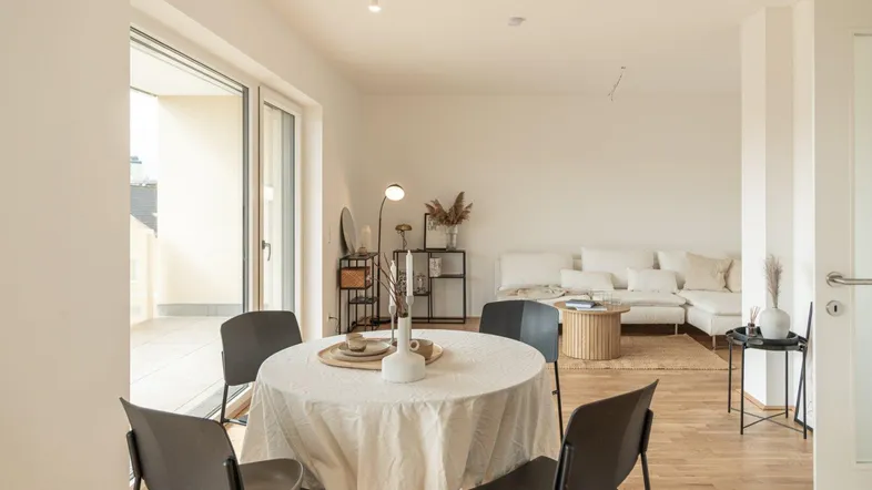 Heller offener Wohn- und Essbereich mit Holzboden und Zugang zum Balkon.