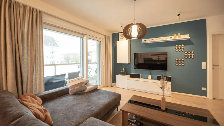 Helles Wohnzimmer mit modernem Sofa, TV-Bereich und Zugang zu einem Balkon.