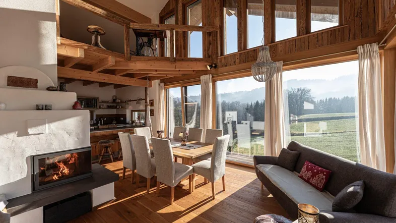 Geräumiger Wohn-Essbereich mit Kamin, Holzbalken und großen Fenstern mit Blick ins Grüne.