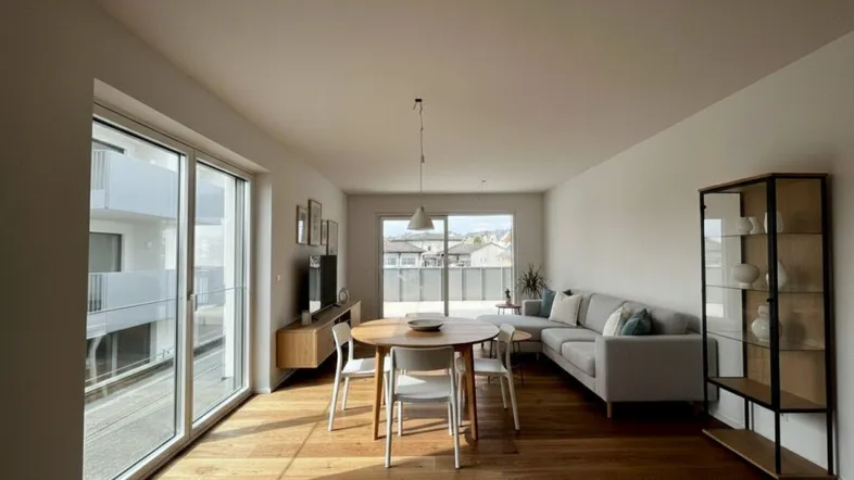 Helles Wohn- und Esszimmer mit Holzboden, großen Fenstern und Zugang zu einem Balkon.