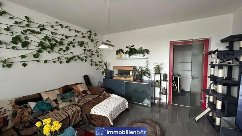 Heller Wohnbereich mit Sofa, Pflanzenwand und Zugang zu einem weiteren Raum.