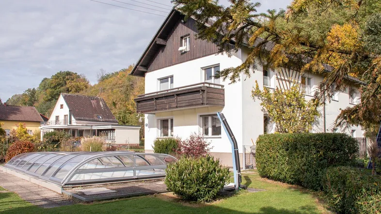 Seitenansicht des Hauses mit Garten, Hecke und einem überdachten Schwimmbecken.
